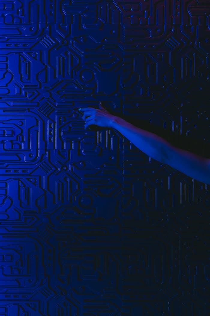 A hand reaches out to touch a futuristic blue circuit patterned wall with dramatic lighting.